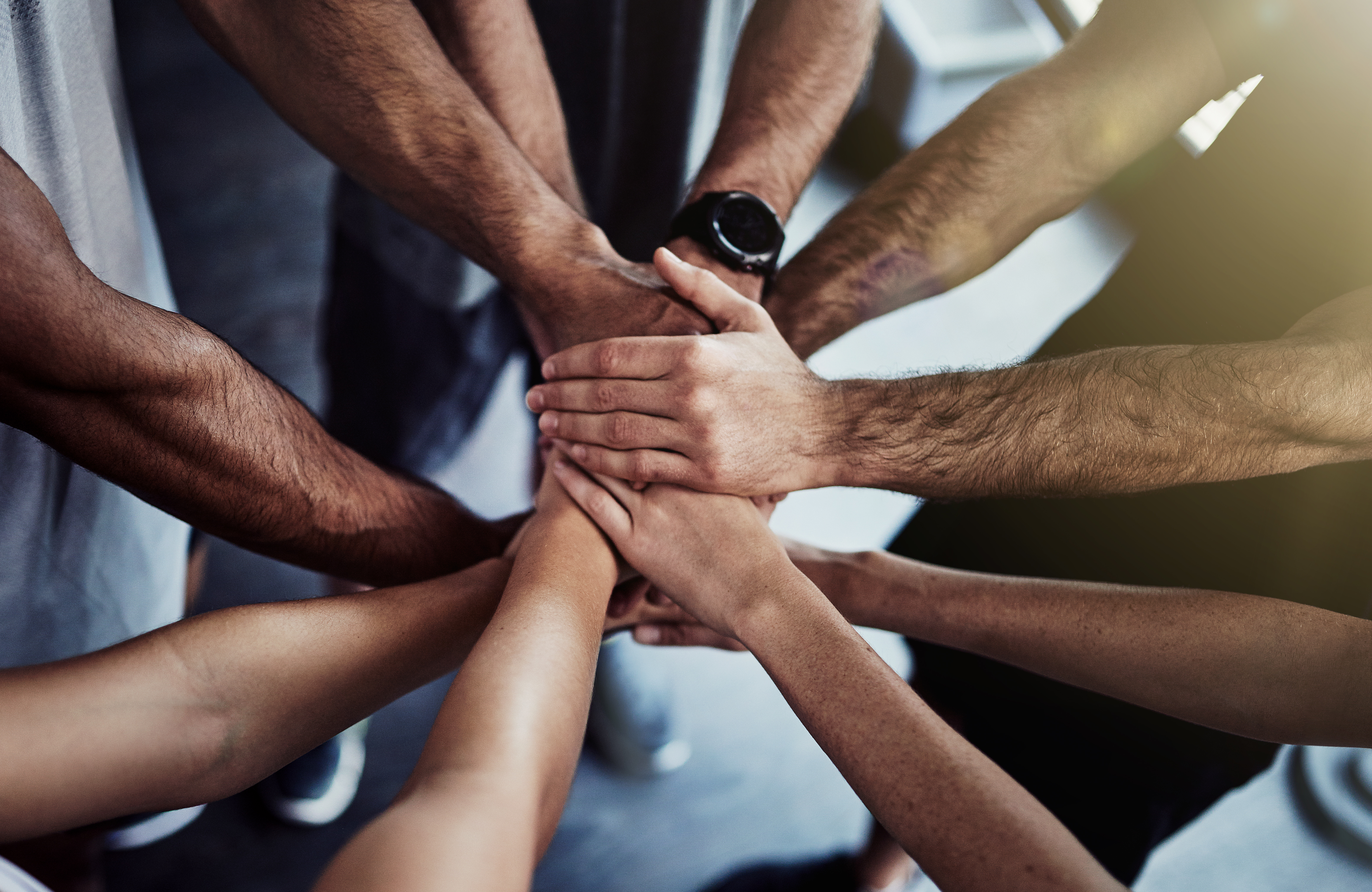 Cropped shot of a group of fit people joining their hands in unity at the gym